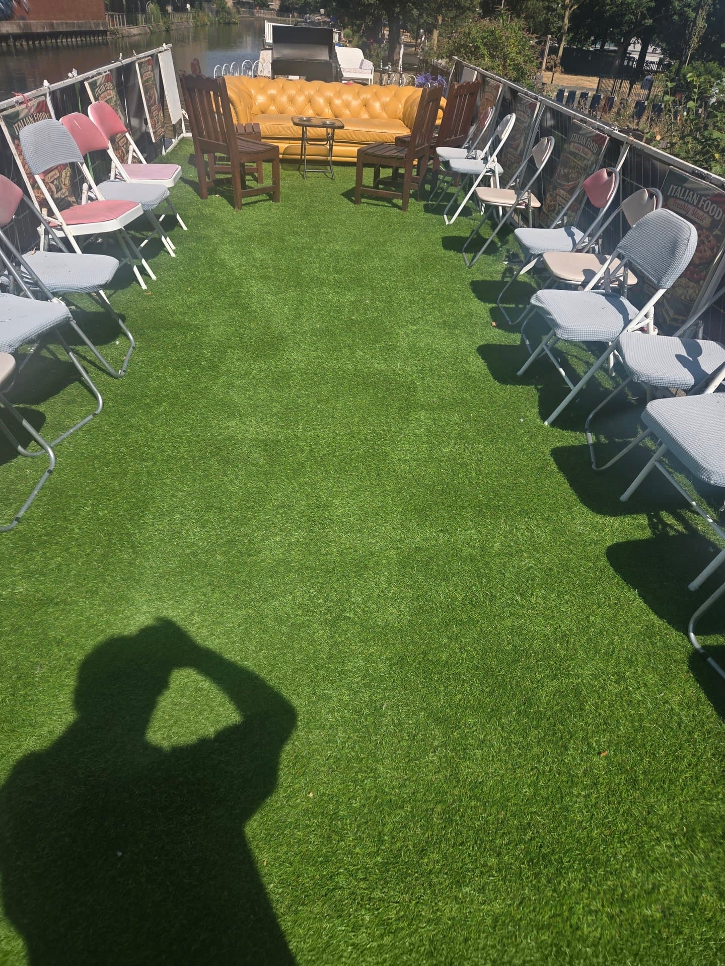 Spacious riverside garden with artificial grass, comfortable seating arrangements and a striking yellow chesterfield sofa, perfect for outdoor entertaining and relaxation.
