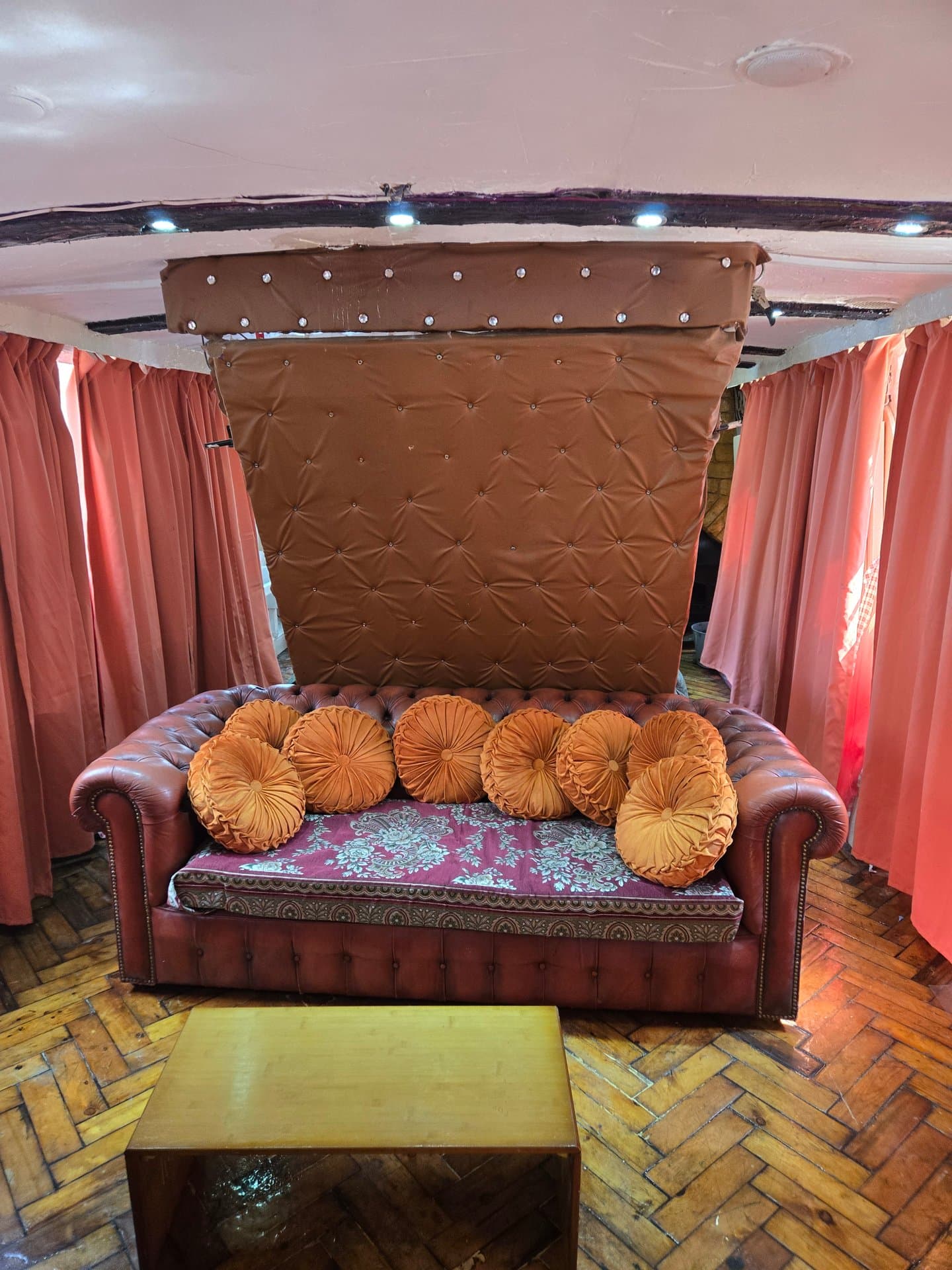 Luxurious four-poster bed with ornate brown headboard, golden scatter cushions, and dramatic draped canopy creating an elegant, theatrical bedroom retreat.