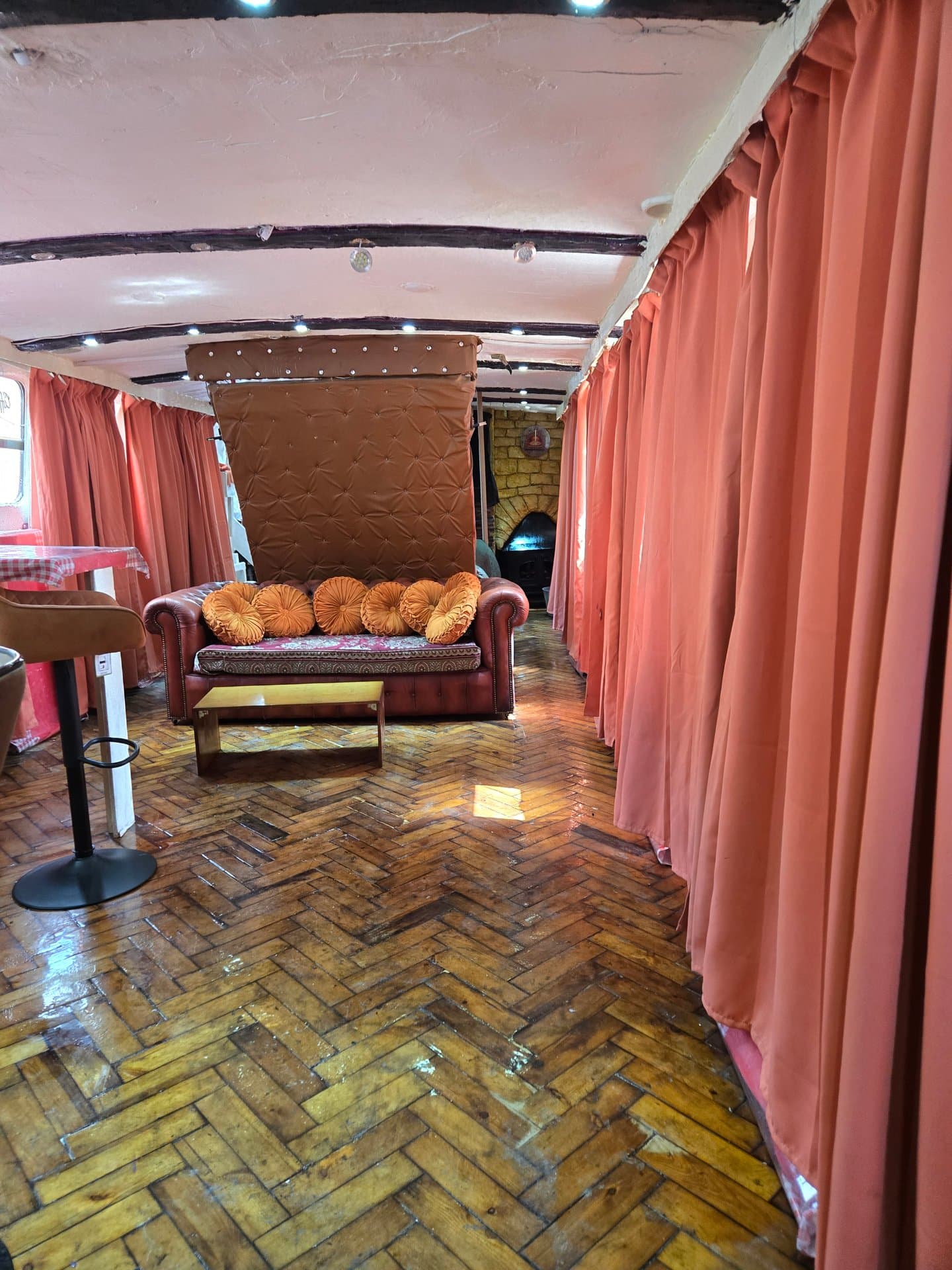 Charming lounge area with vintage Chesterfield sofa, decorative cushions, and warm ambient lighting. Red velvet curtains create an intimate, sophisticated atmosphere perfect for relaxation.